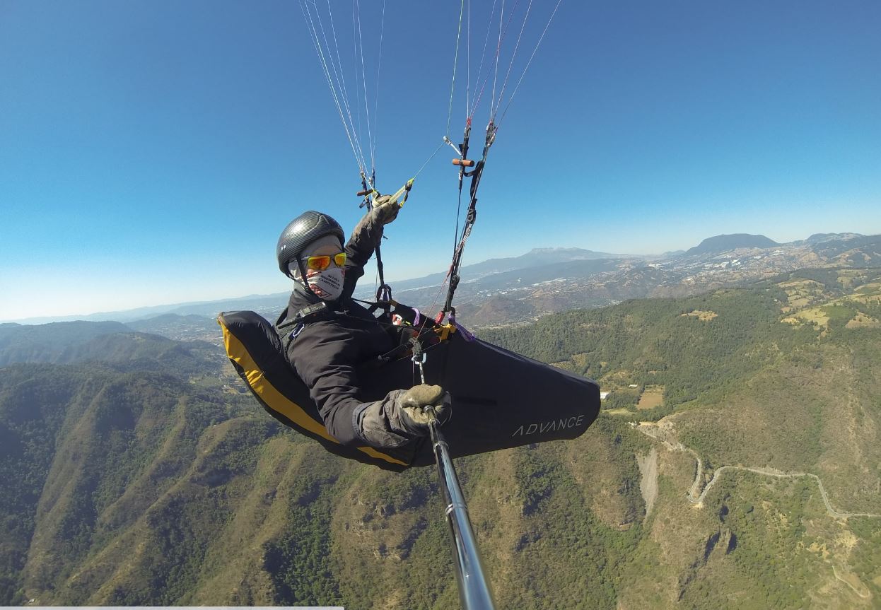 Paraglider flying over lush green terrain
